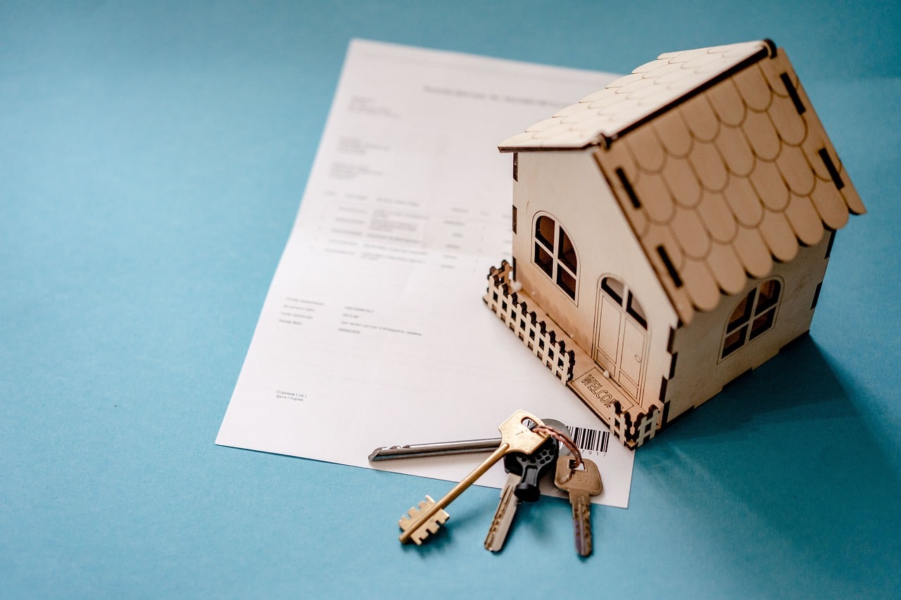 A paper model of a house and keys sitting on a contract
